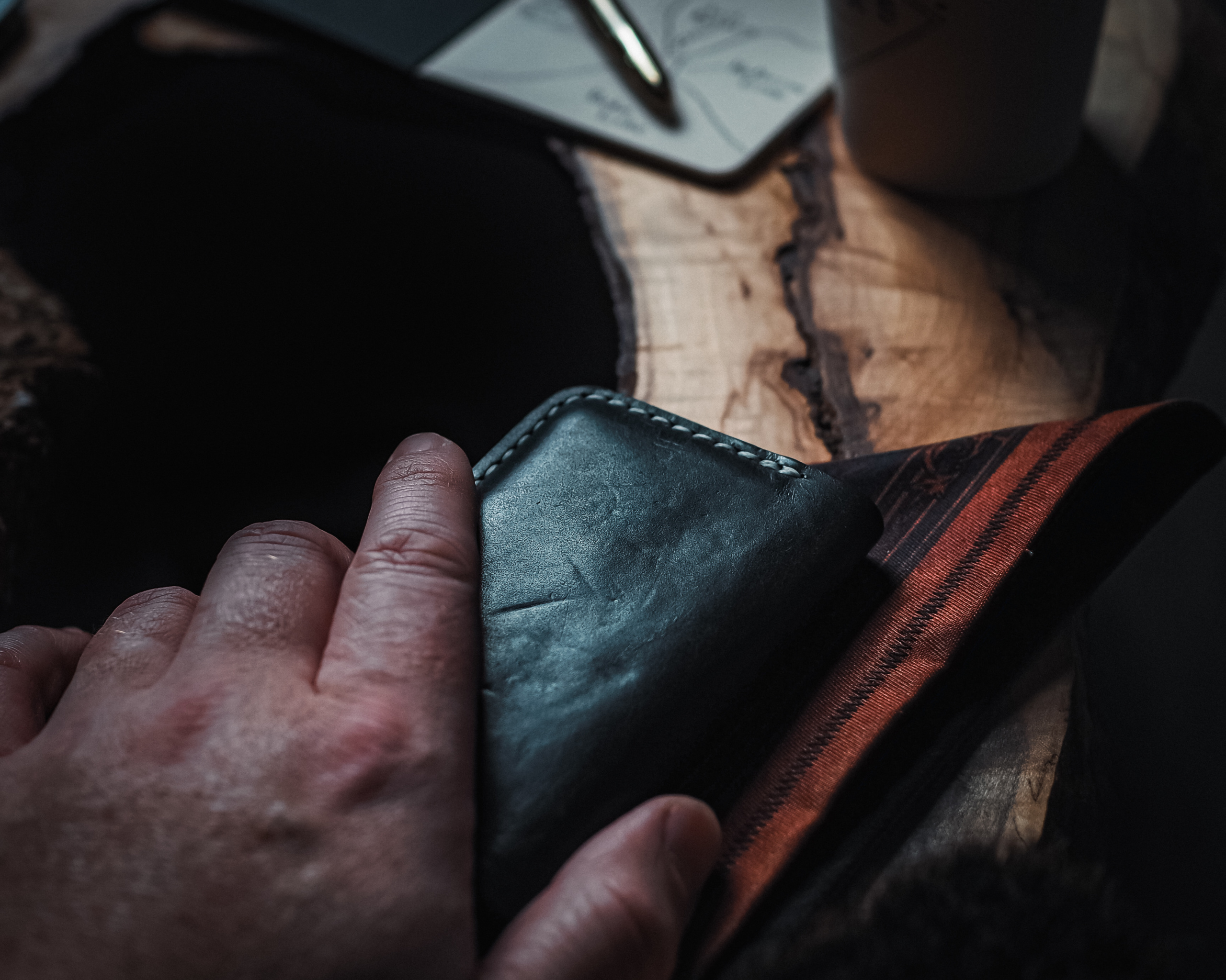 Hand holding a leather wallet in front of a notebook and coffee